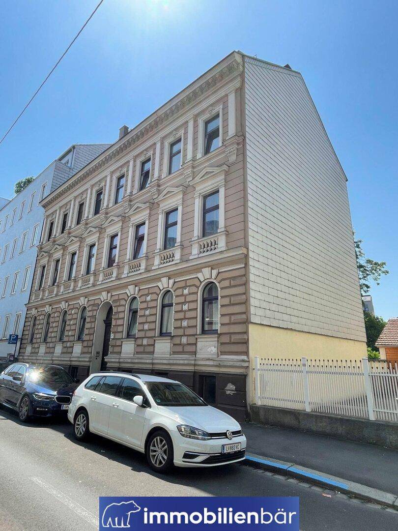 Historische Fassade eines Altbaus mit dekorativen Elementen und parkenden Autos davor.