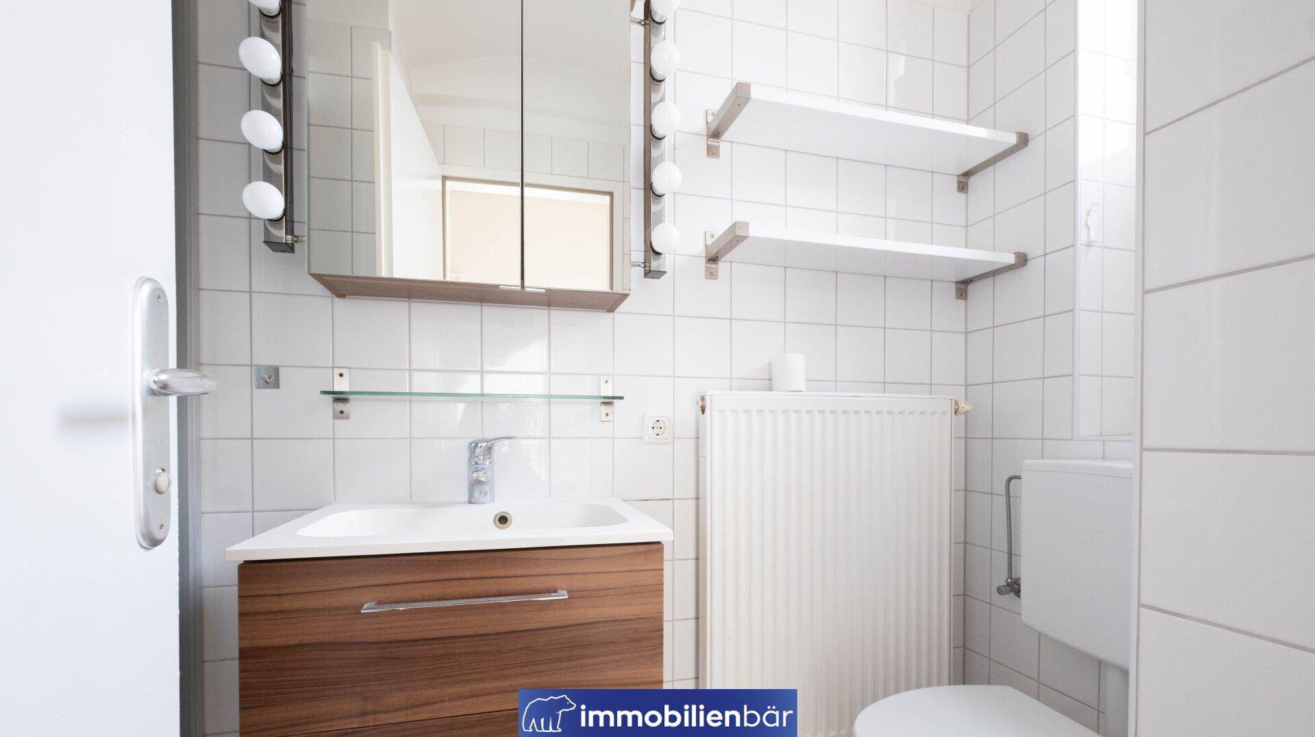 Modernes Badezimmer mit weißen Fliesen, Waschbeckenunterschrank und Spiegelschrank.