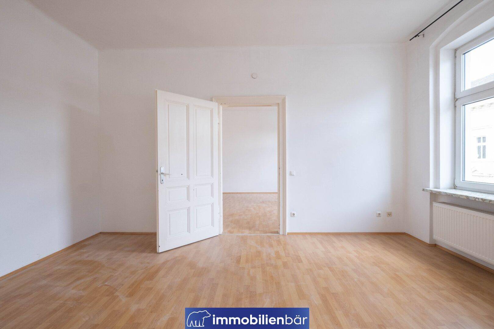 Helles Zimmer mit Parkettboden und einem großen Fenster, das viel Tageslicht bietet.
