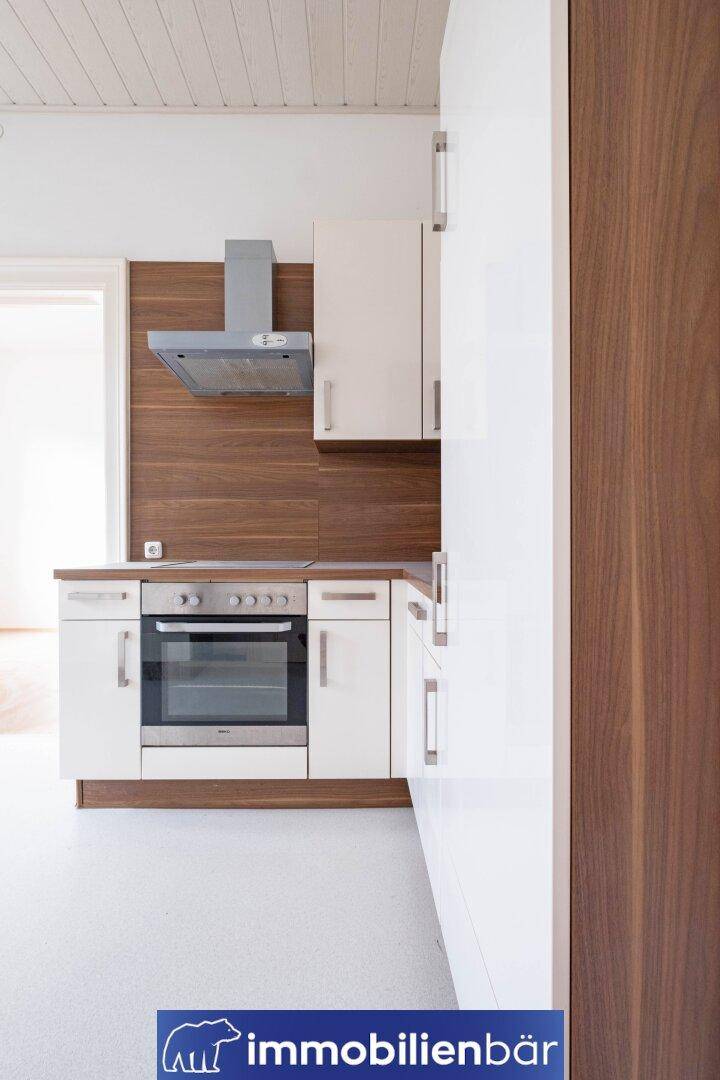 Moderne Küchenzeile mit weißen Schränken, Holzakzenten und integriertem Backofen.