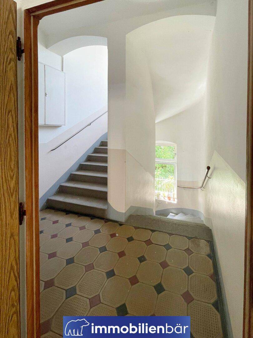 Helles Treppenhaus mit originalen Fliesen und einem Fenster, das Tageslicht hereinlässt.