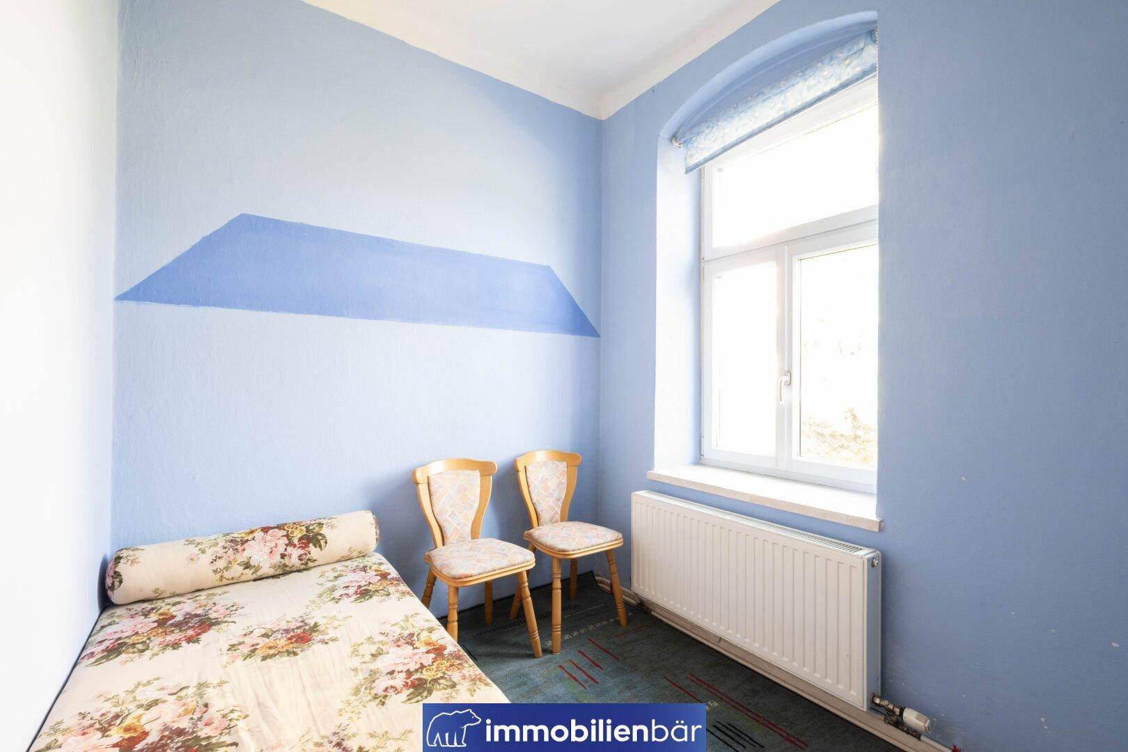 Helles Zimmer mit blau gestrichenen Wänden, Einzelbett und großem Fenster.