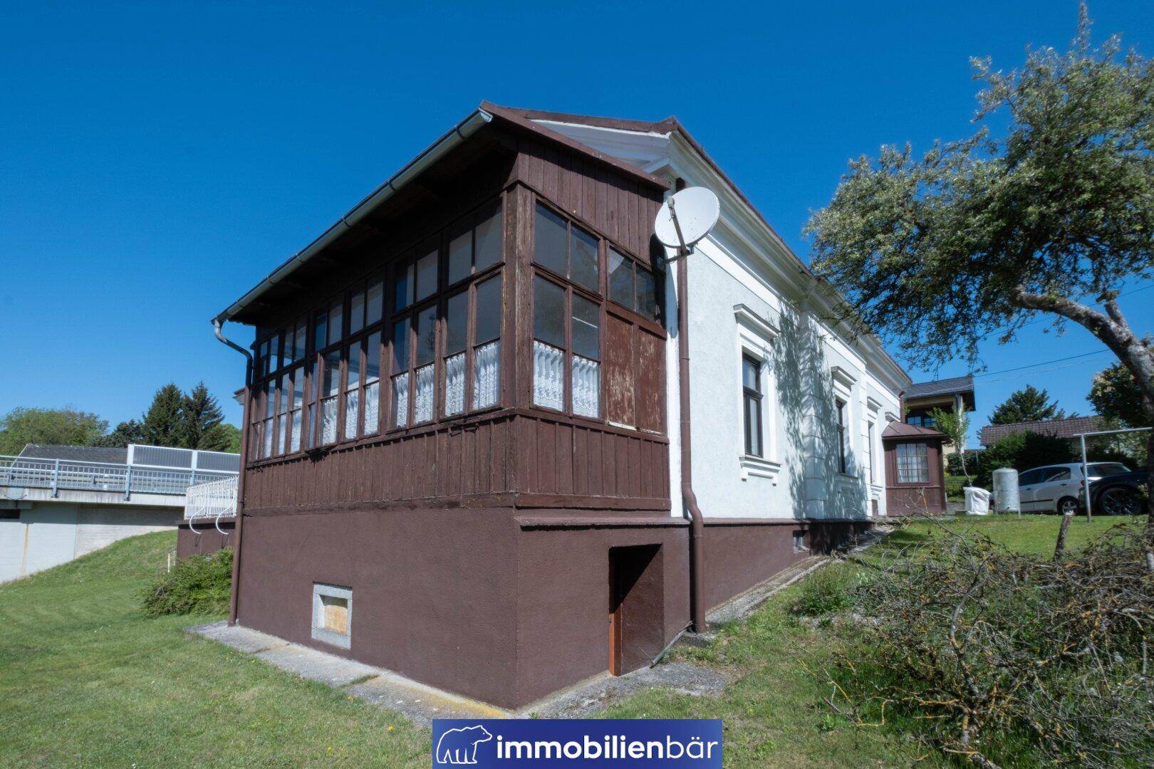 Seitenansicht des Hauses mit verglastem Anbau und Satellitenschüssel an der Fassade.