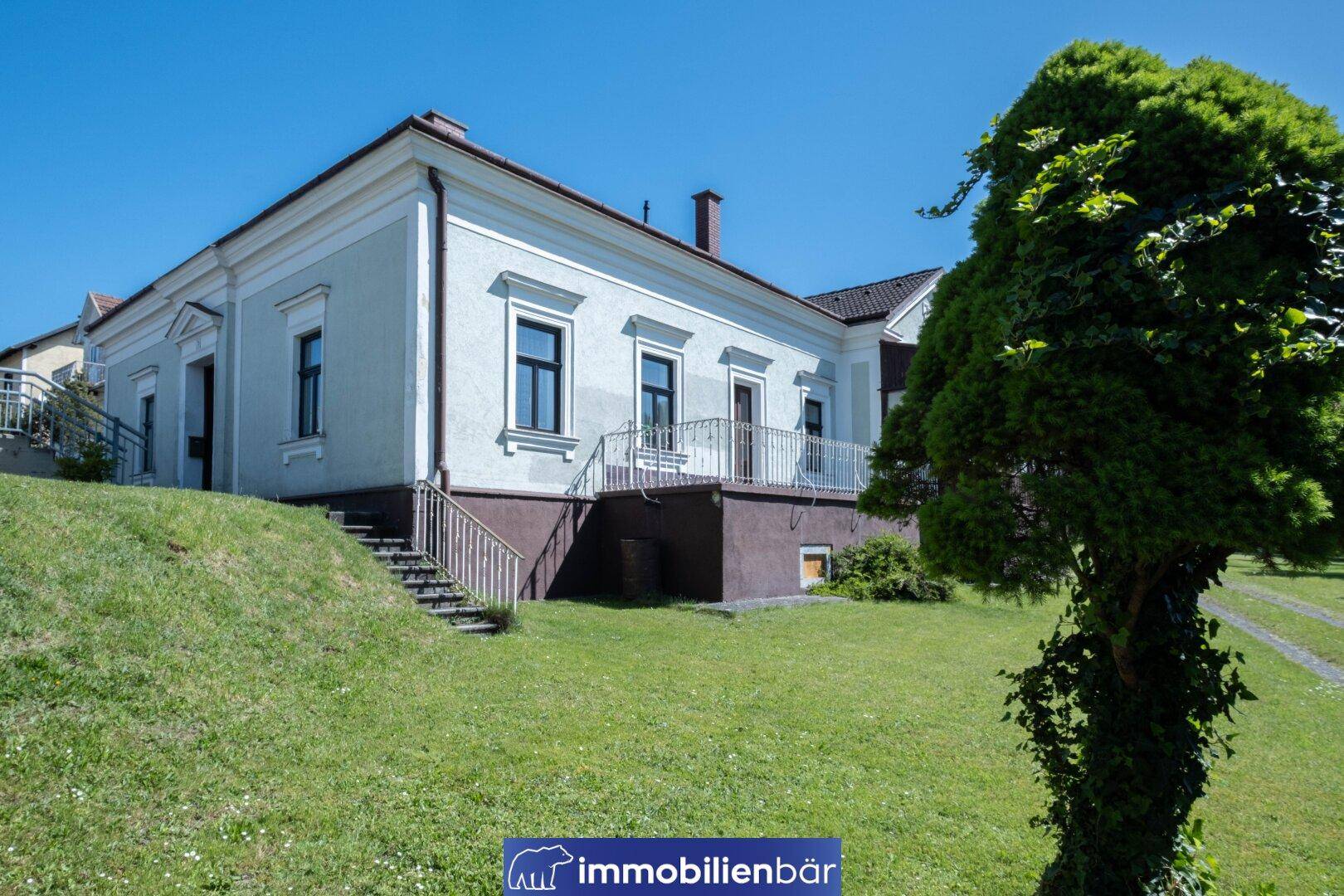 Seitenansicht des Wohnhauses mit Treppe zum Eingang und weitläufiger Rasenfläche.