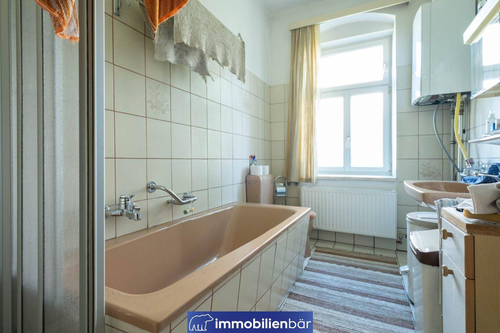 Badezimmer mit beigefarbener Badewanne, Fliesen und Fenster für Tageslicht.