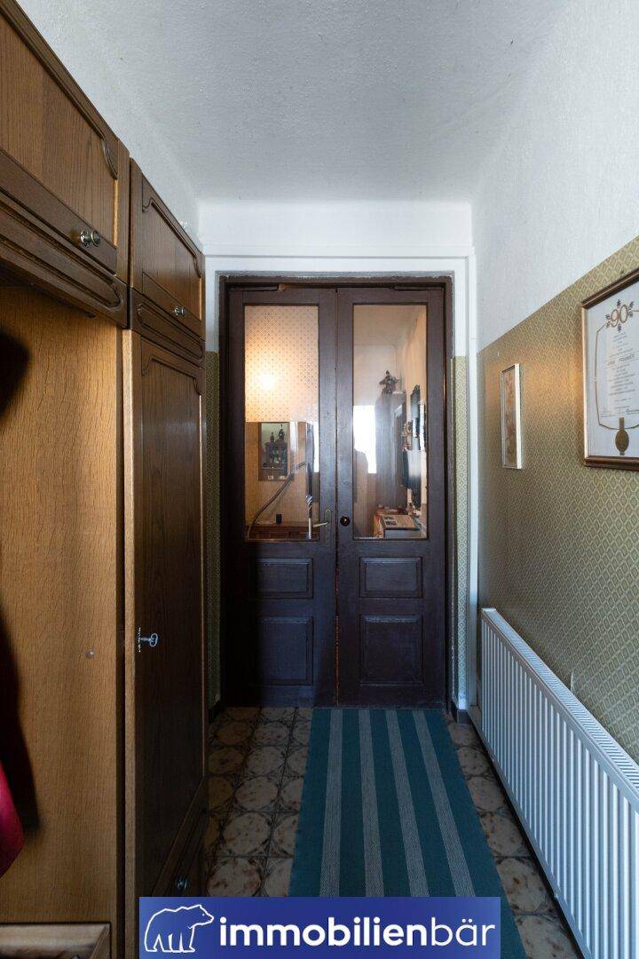 Flur mit gemustertem Teppich, Heizkörper und Holztüren mit Glaseinsätzen.