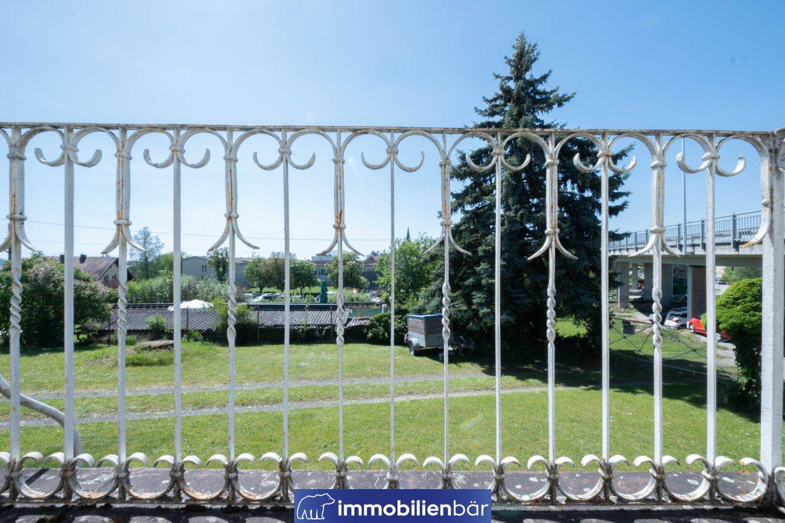 Blick über ein schmiedeeisernes Geländer auf den grünen Garten und die Umgebung.