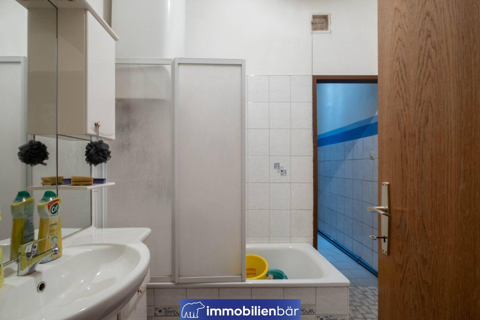 Badezimmer mit Duschwanne, Waschbecken und weißen Fliesen an den Wänden.