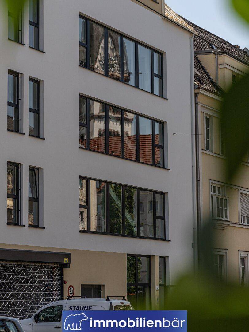 Detailansicht der modernen Fassade mit großen Fenstern, die eine Kirche und Bäume spiegeln.