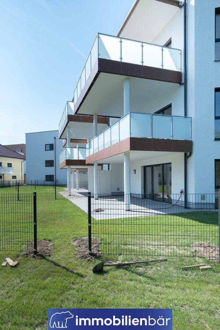 Rückseite eines modernen Wohngebäudes mit Balkonen, Terrassen und eingezäuntem Gartenbereich.