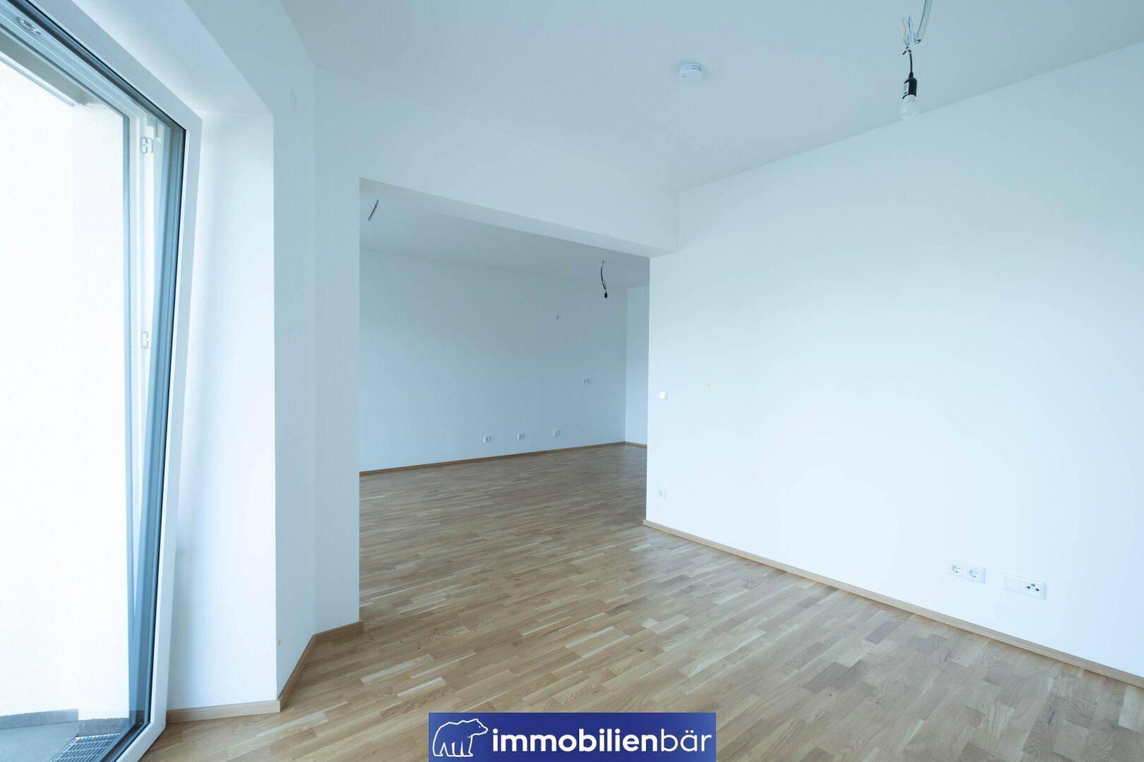 Geräumiges, helles Zimmer mit Parkettboden und viel Tageslicht durch die große Tür.