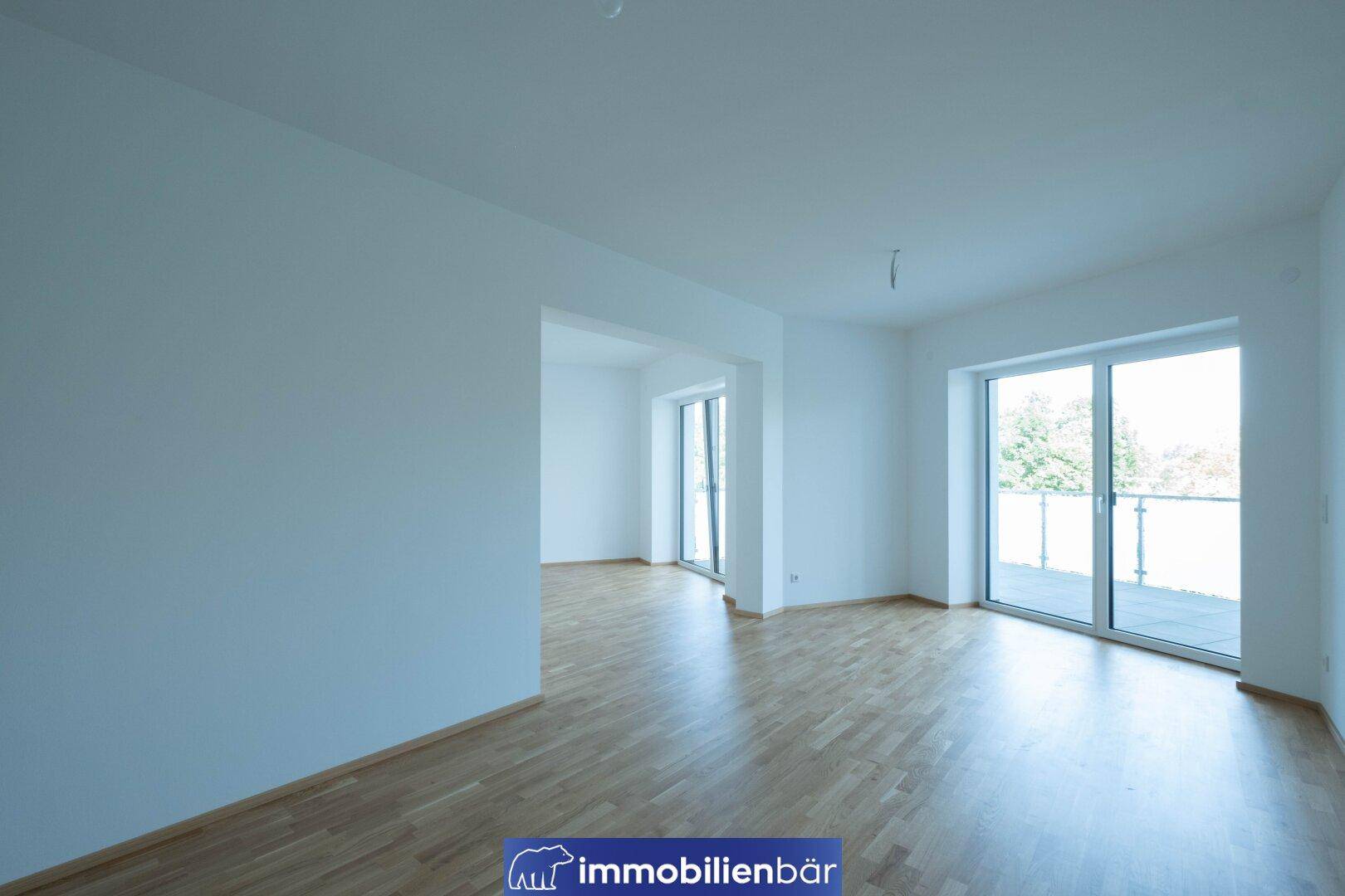 Geräumiges, unmöbliertes Zimmer mit hellem Parkettboden und Zugang zum Außenbereich.