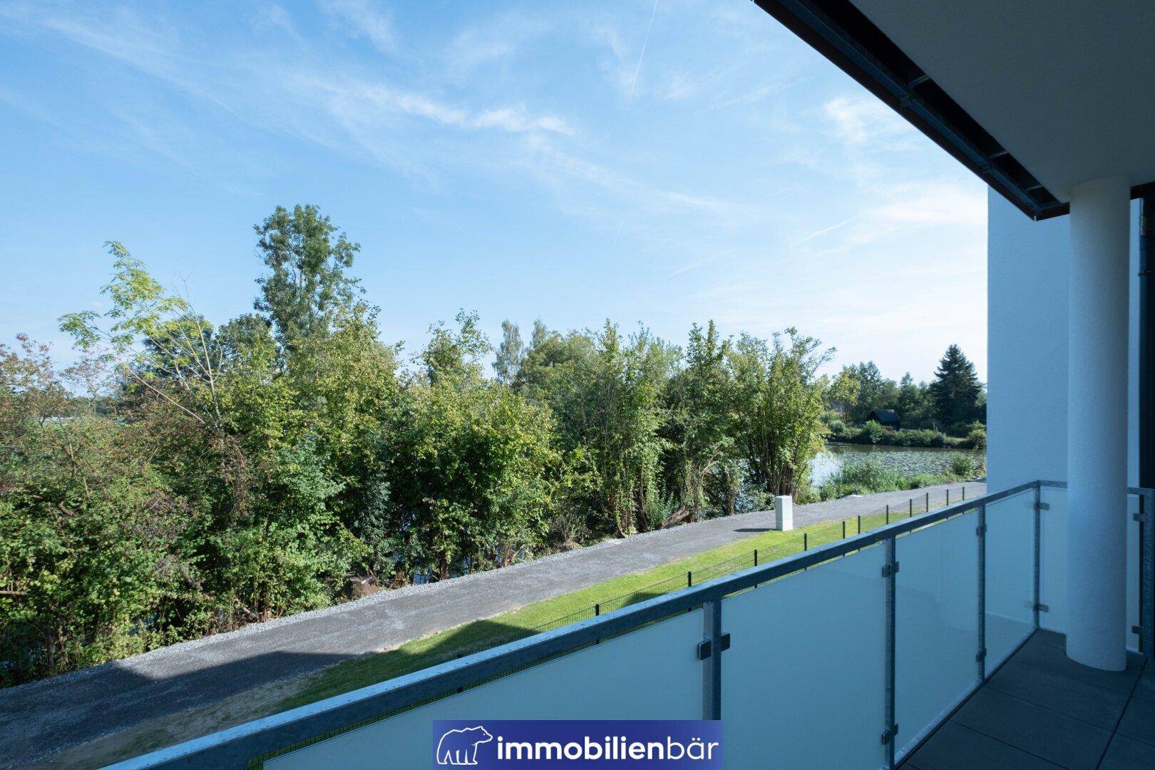 Balkon mit Fliesenboden und Glasbrüstung, bietet einen Ausblick auf Bäume und Wasser.