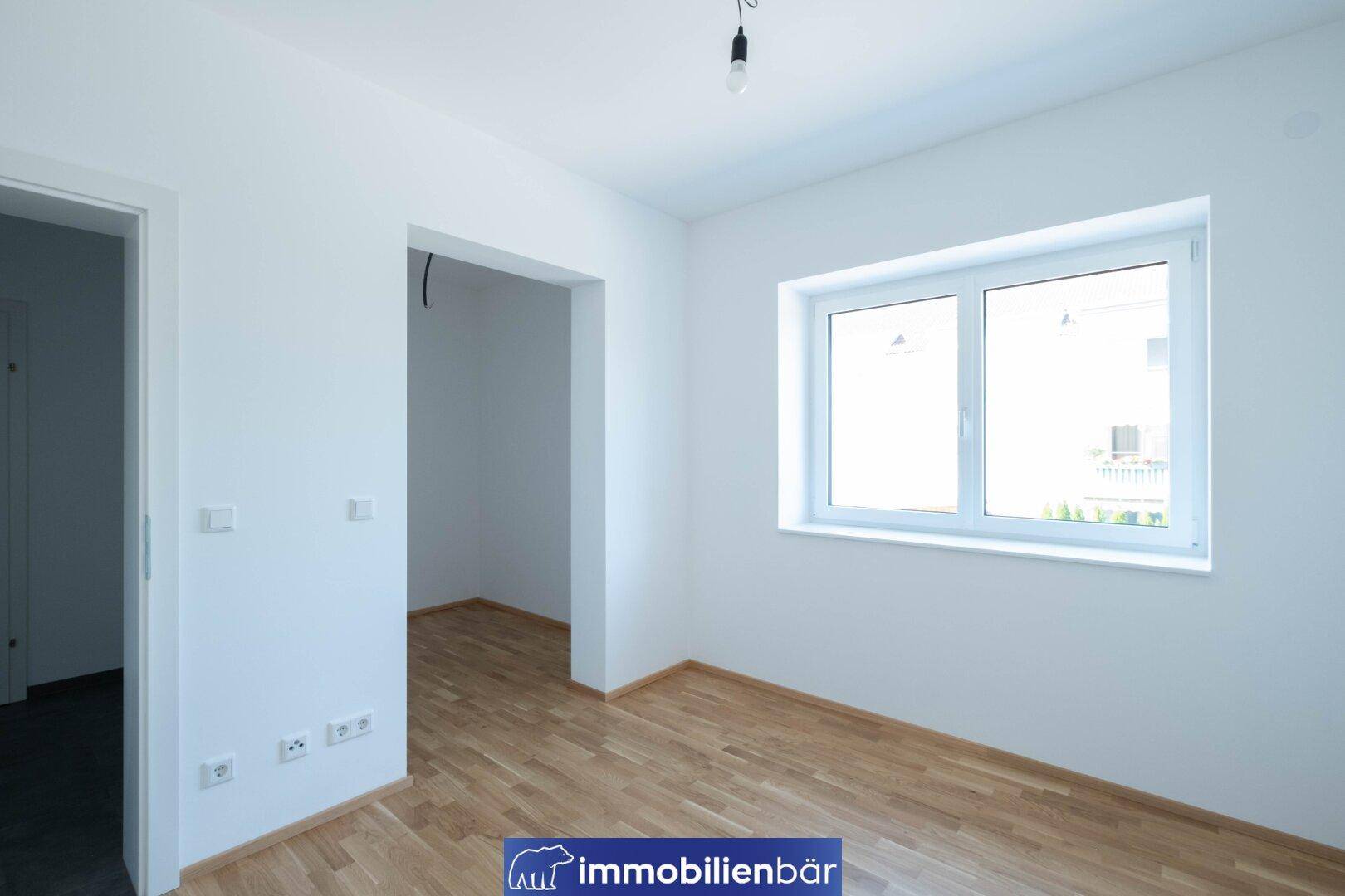 Helles, unmöbliertes Zimmer mit Parkettboden und einem großen Fenster.