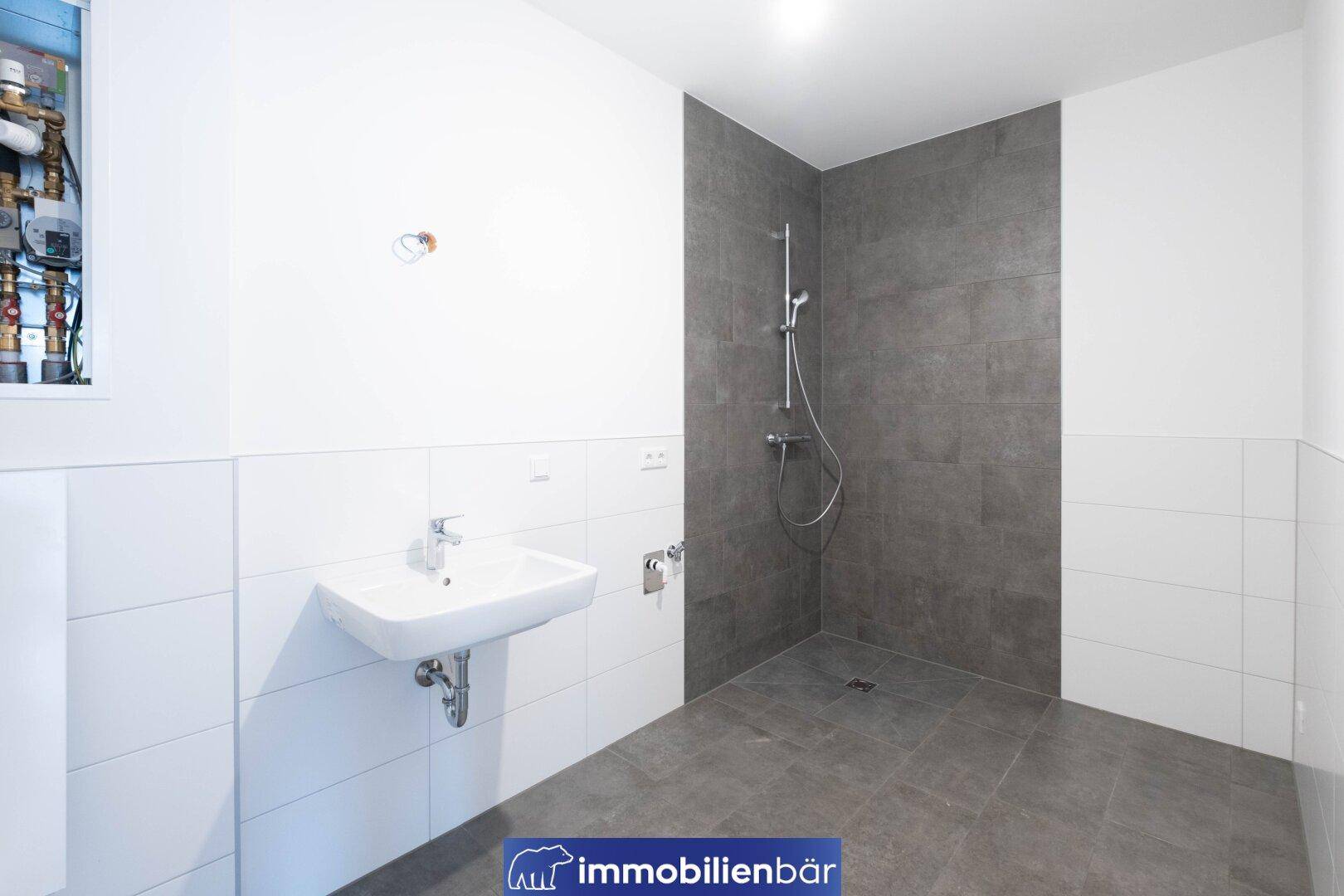 Modernes Badezimmer mit Einzelwaschbecken, großer Duschfläche und grauen Fliesen.