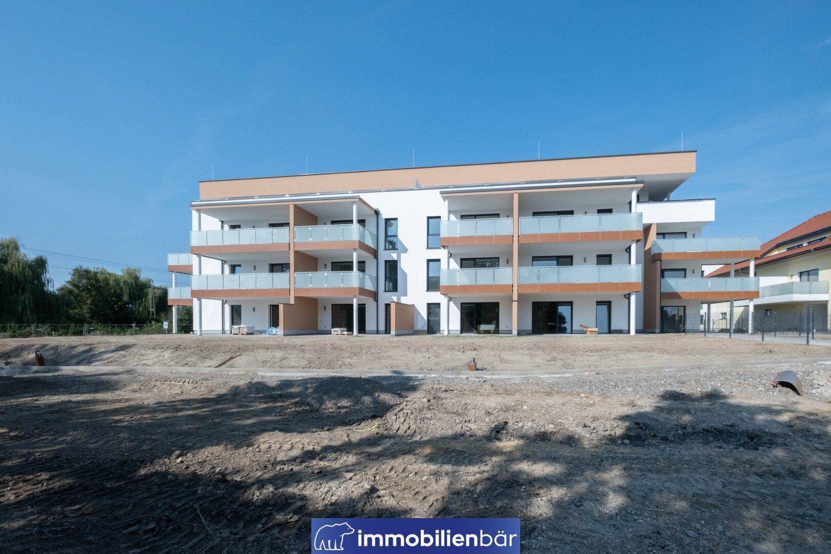 Modernes Mehrfamilienhaus im Bau mit Balkonen und Terrassen in ländlicher Umgebung.