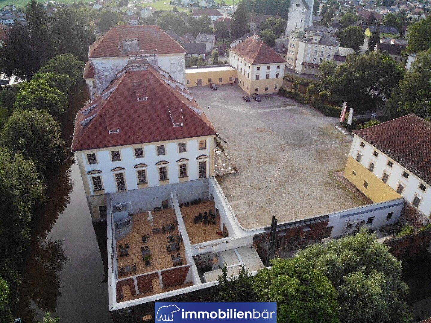 Luftaufnahme des weitläufigen Schlosskomplexes mit Innenhof, umgeben von Wasser und Grünflächen.