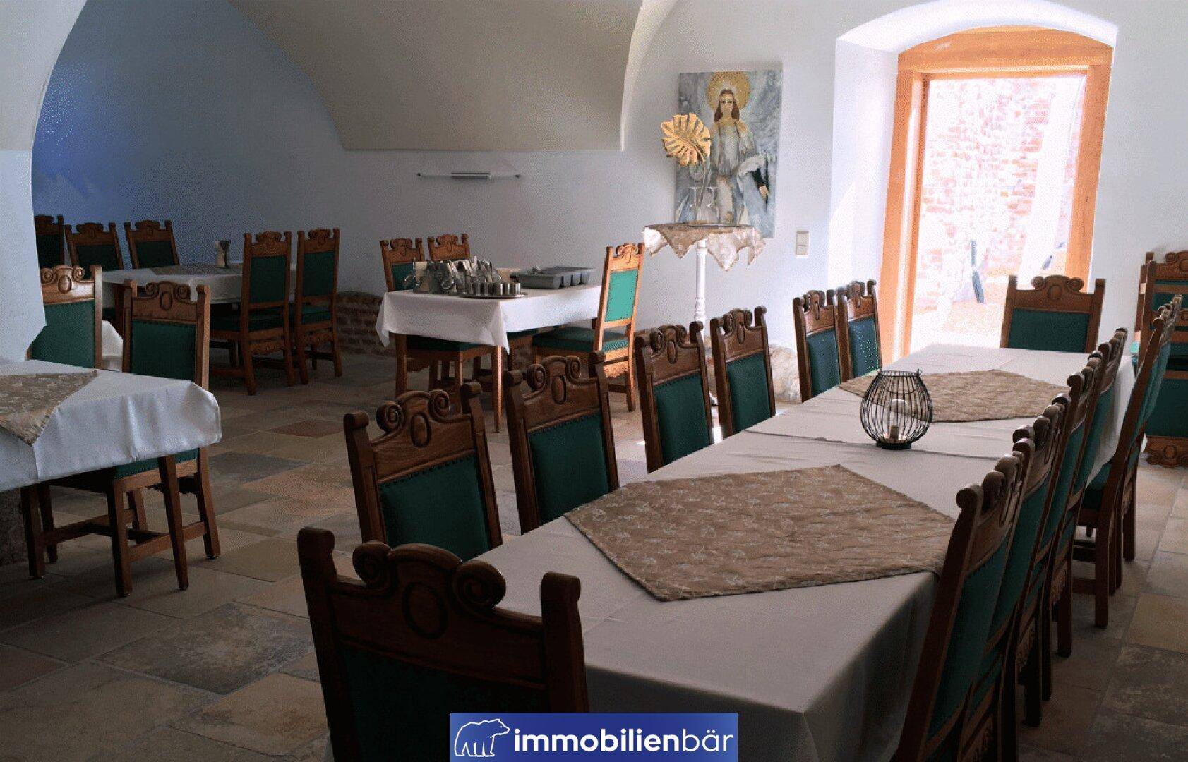 Traditioneller Speisesaal mit langen Tischen, holzgeschnitzten Stühlen und gefliestem Boden in historischem Ambiente.