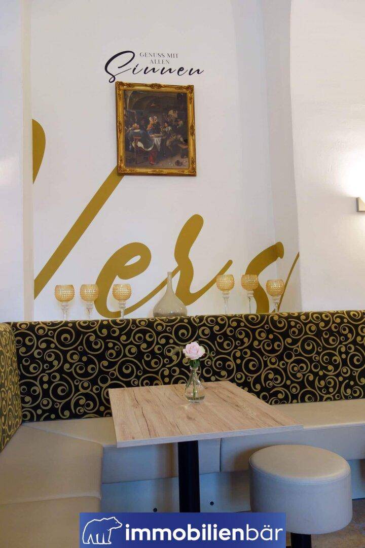 Gemütliche Sitzecke in einem Restaurant mit gepolsterter Bank, Holztisch und dekorativer Wandgestaltung.