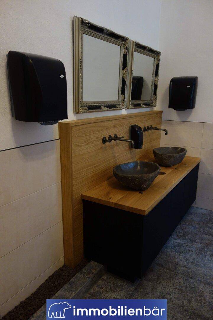 Modern gestalteter Waschraum mit zwei Steinwaschbecken auf Holzplatte und großen Spiegeln.