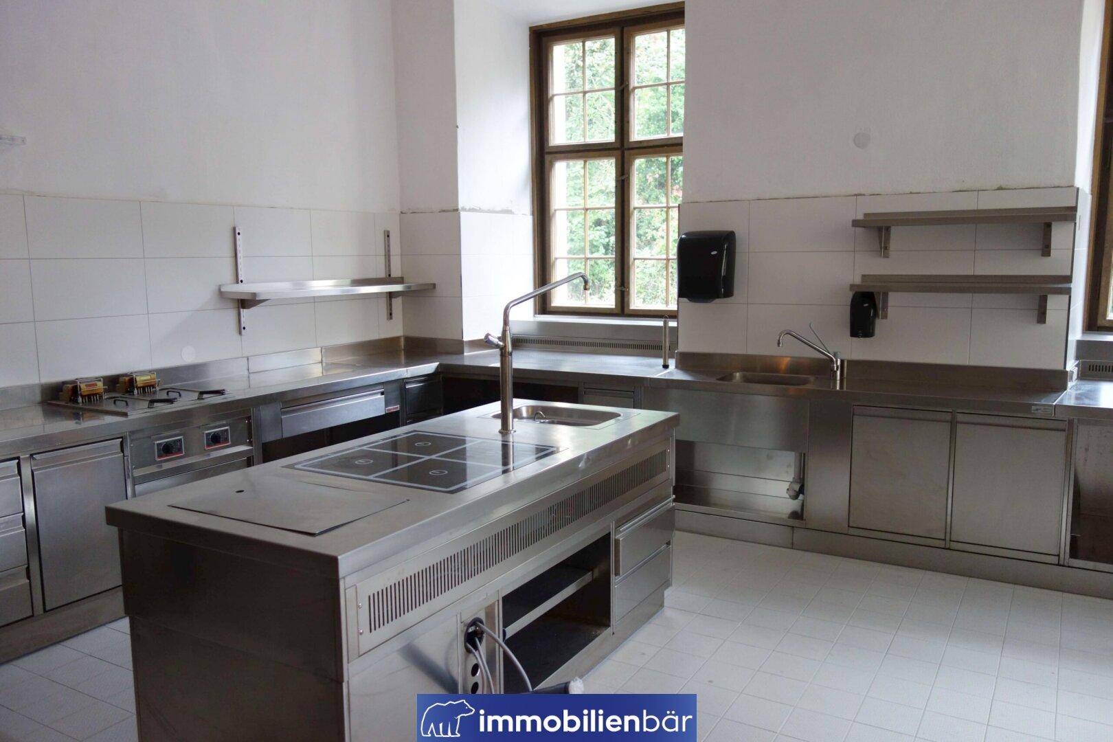 Professionelle Edelstahlküche mit Kochinsel, mehreren Spülbecken und Arbeitsflächen für Gastronomiebetriebe.