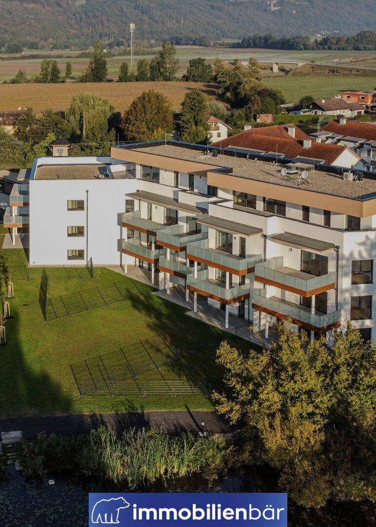 Modernes Wohngebäude mit Balkonen, gepflegtem Rasen und angrenzendem Teich.