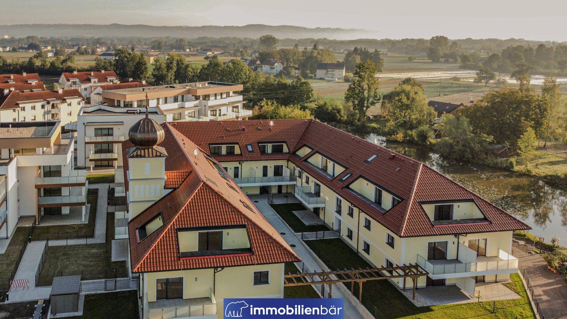 Vogelperspektive auf einen Wohnkomplex mit traditionellem Gebäude, modernen Bauten und Teich.