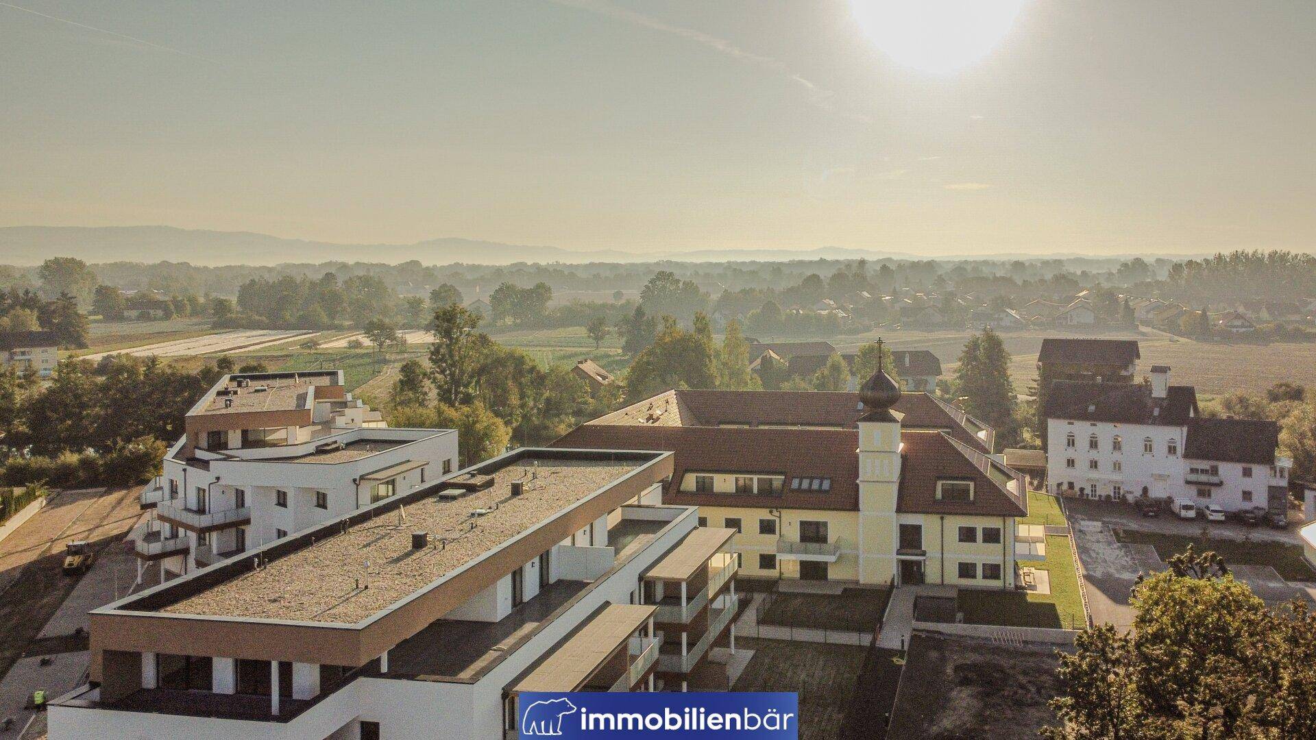 Weitläufige Ansicht eines Wohnkomplexes mit modernen und traditionellen Gebäuden in ländlicher Umgebung.