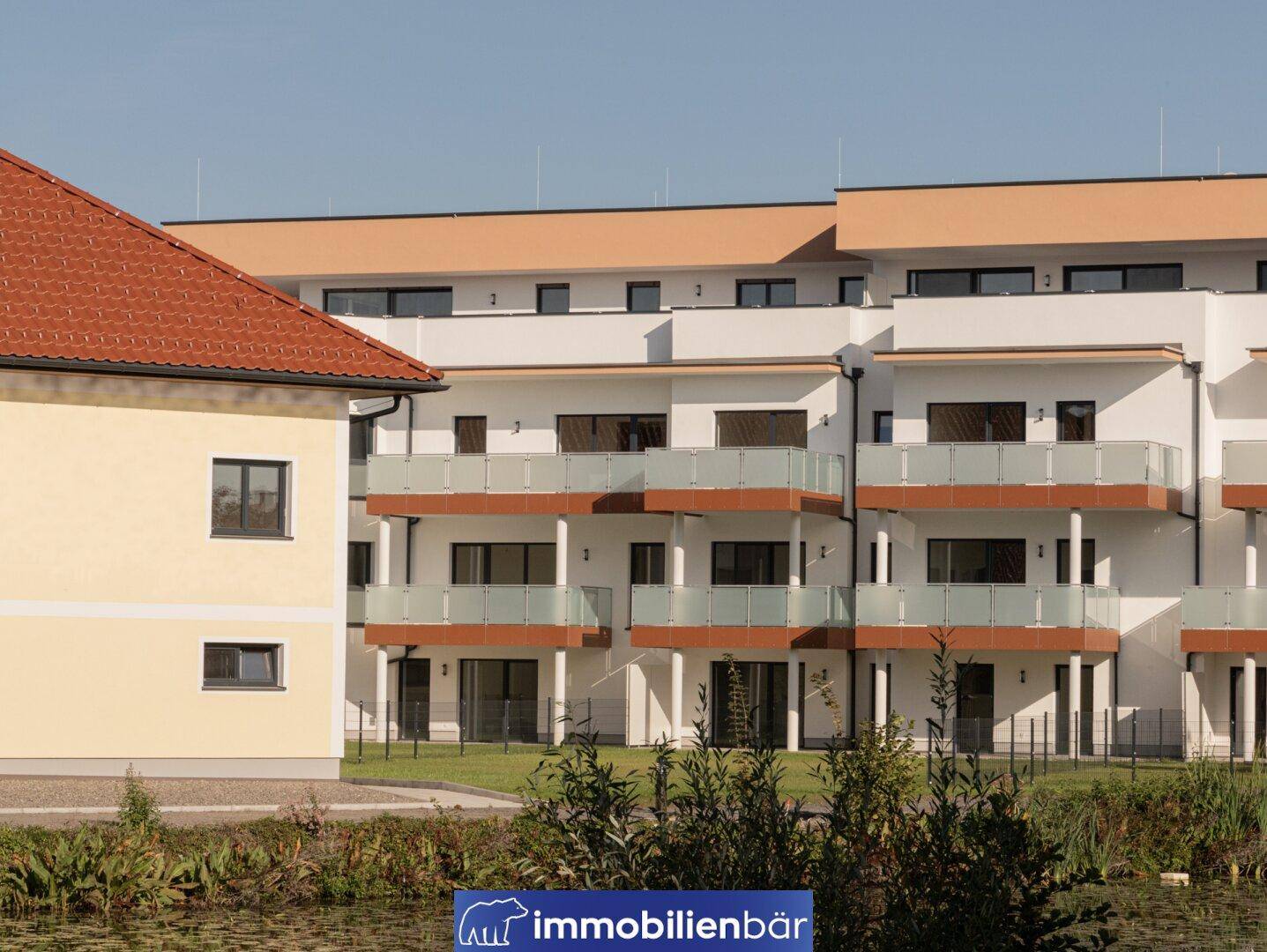 Modernes Wohngebäude mit Balkonen und Blick auf den angrenzenden Teich.