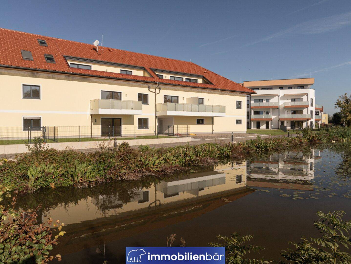 Wohngebäude mit rotem Ziegeldach und modernen Balkonen am Teichufer.