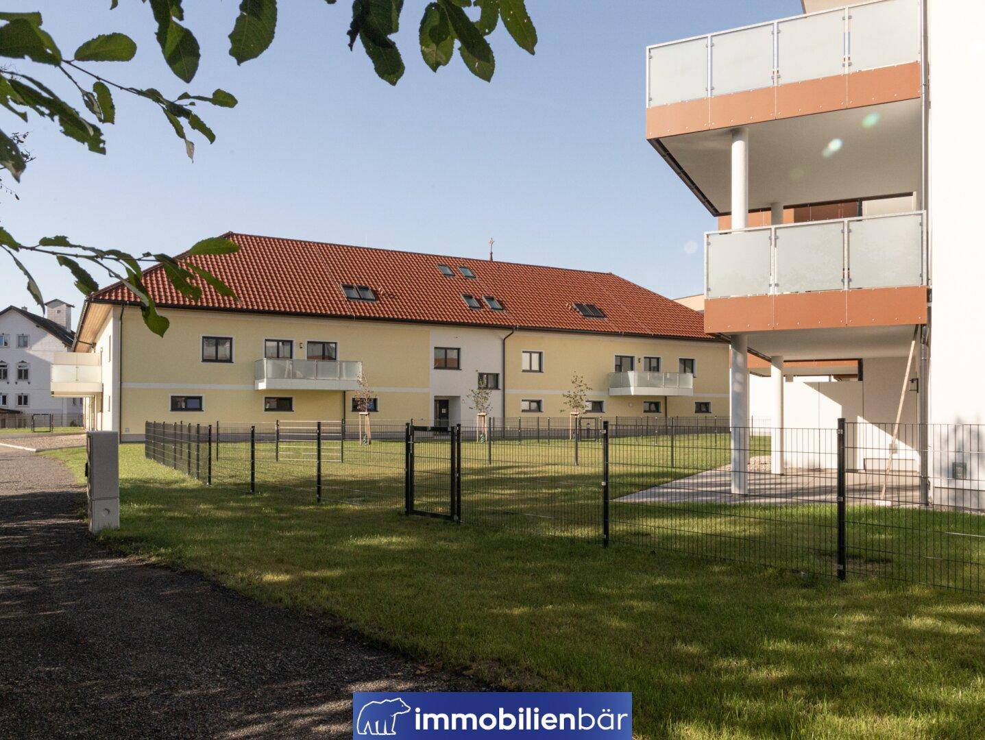 Modernes Wohngebäude mit Balkonen und einem weitläufigen, eingezäunten Rasenbereich.