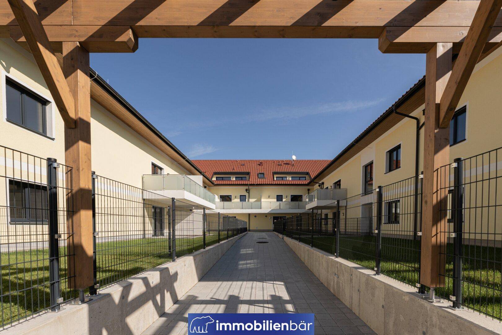 Innenhof mit gepflastertem Weg und Pergola, umgeben von Wohngebäuden.