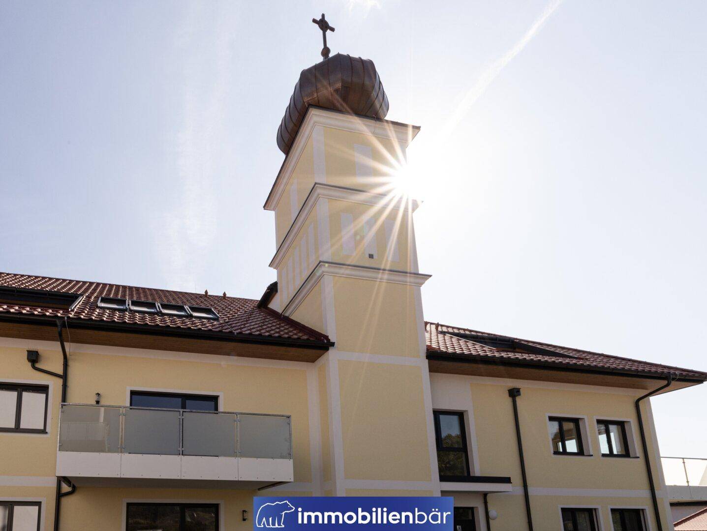 Detailansicht eines Gebäudes mit traditionellem Turm und Balkon unter strahlendem Sonnenschein.