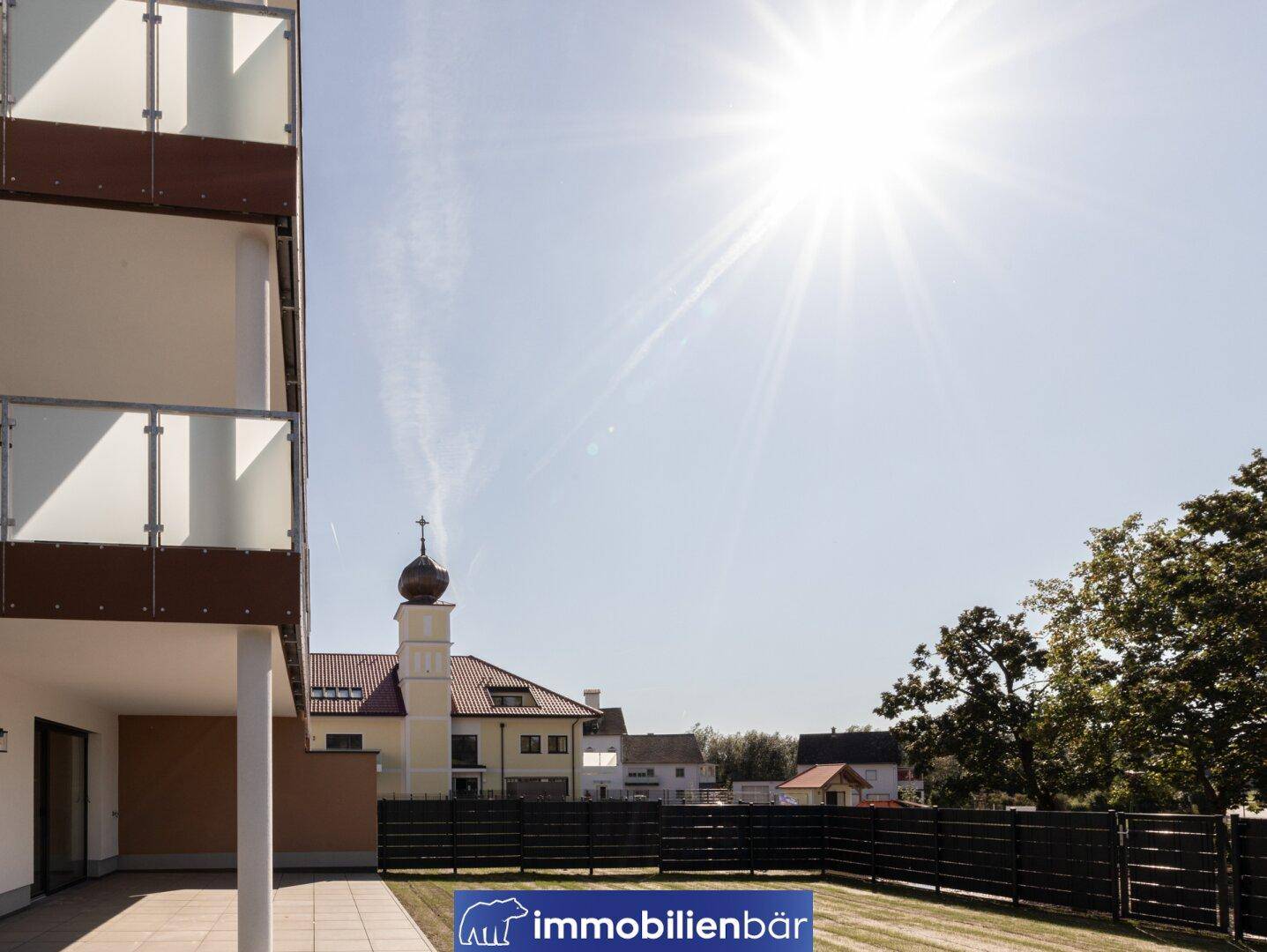 Sonnenbeschienener Terrassenbereich mit angrenzendem Rasen und Blick auf das traditionelle Gebäude.