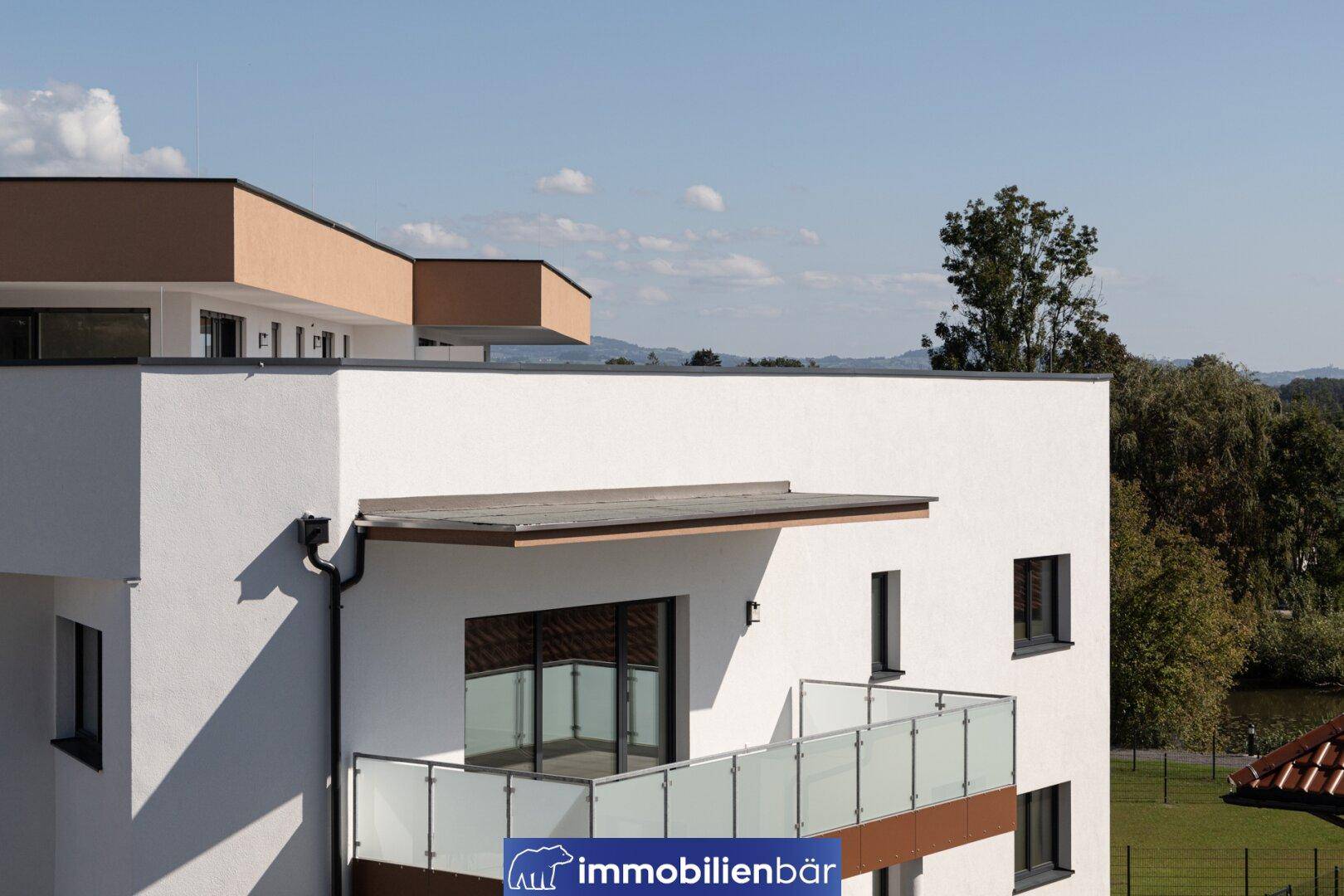 Modernes Wohngebäude mit Balkon und Blick auf die grüne Umgebung und den Teich.