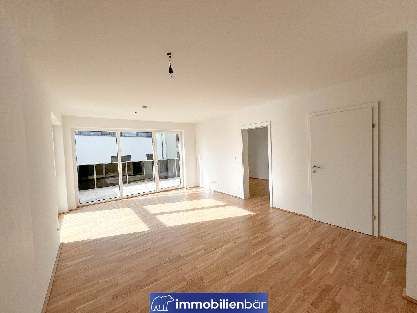 Geräumiges Wohnzimmer mit hellem Parkettboden und viel Tageslicht durch große Fenster.