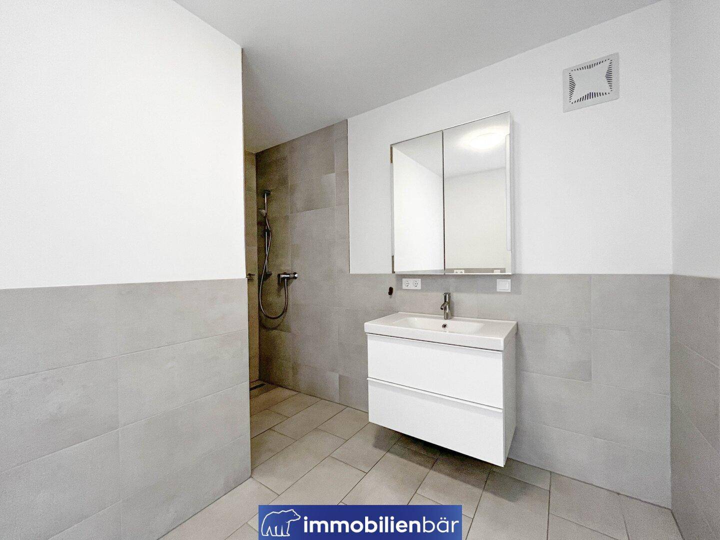 Modernes Badezimmer mit Dusche, Waschtisch und Spiegelschrank in hellen Grautönen.