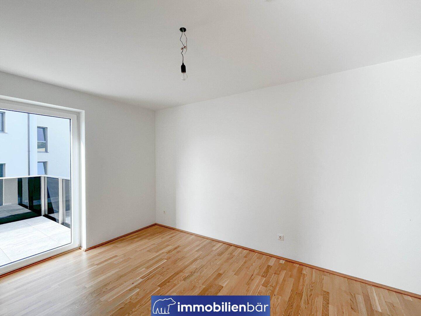 Helles Schlafzimmer mit Parkettboden und direktem Zugang zu einem Balkon.