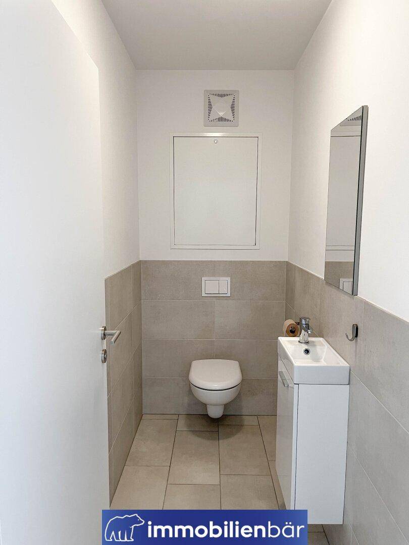 Modernes Gäste-WC mit wandhängendem WC, kleinem Waschbecken und Fliesenboden.
