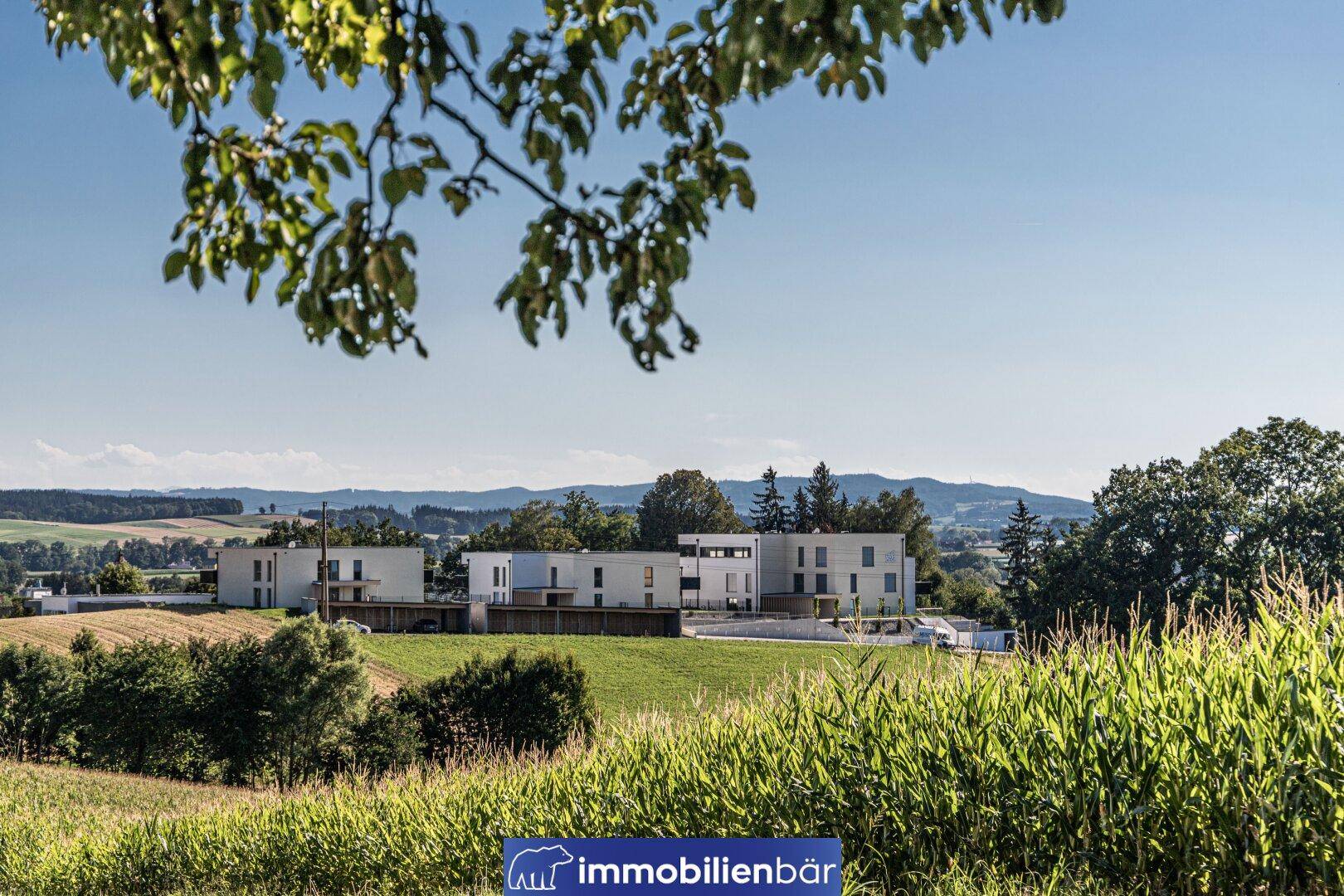 Weitläufiger Blick auf die neuen Wohngebäude, eingebettet in die grüne Hügellandschaft und ländliche Umgebung.