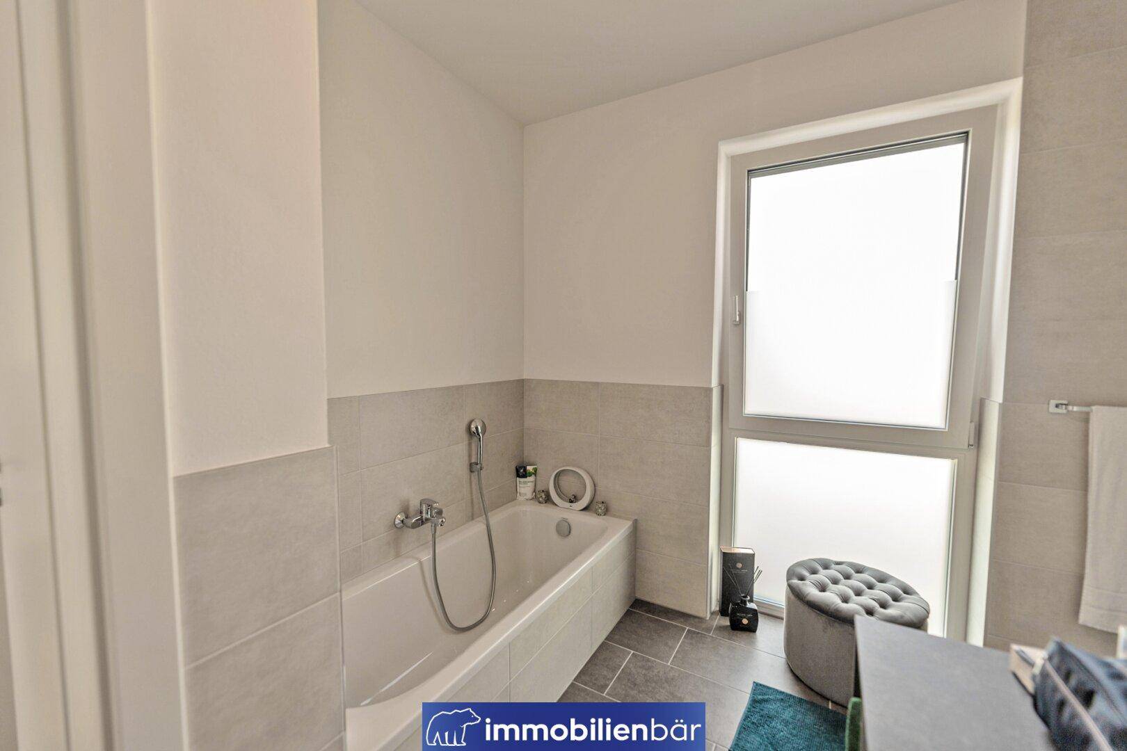 Modernes Badezimmer mit Badewanne, hellen Fliesen und einem Fenster für natürliche Belüftung und Tageslicht.