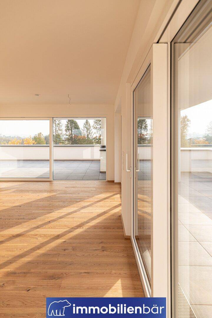 Lichtdurchfluteter Raum mit Holzboden und breiten Fenstertüren, die Zugang zur Außenterrasse bieten.