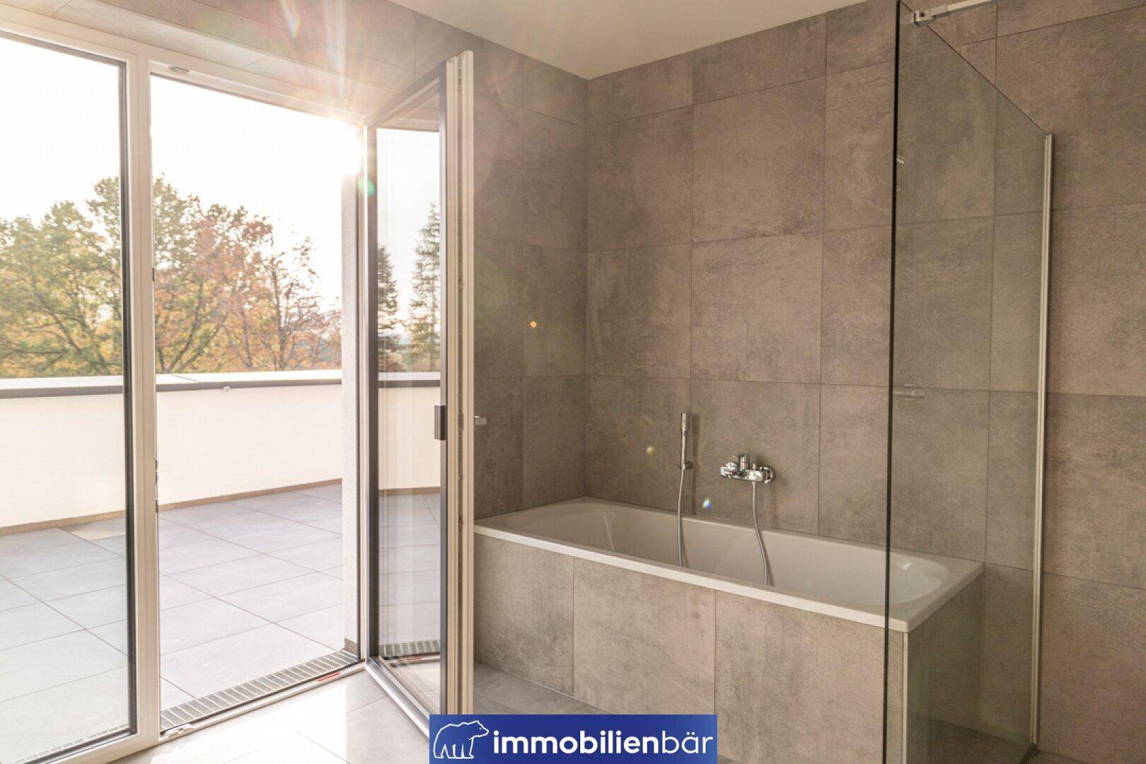 Modernes Badezimmer mit Badewanne, Duschabtrennung und großen Fenstertüren zur Terrasse.