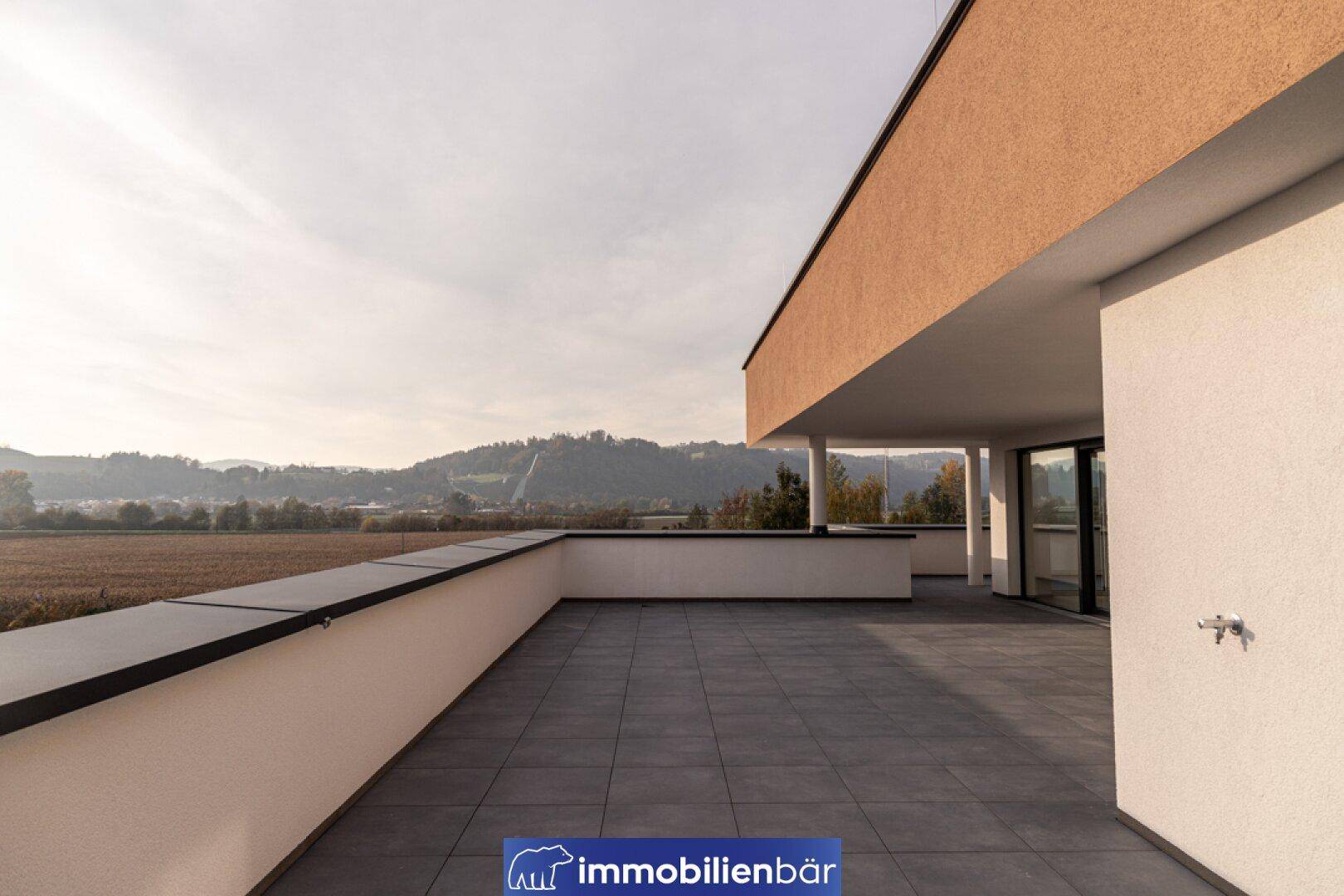 Große, geflieste Terrasse mit niedriger Brüstung und weitem Blick auf die umliegende Landschaft.