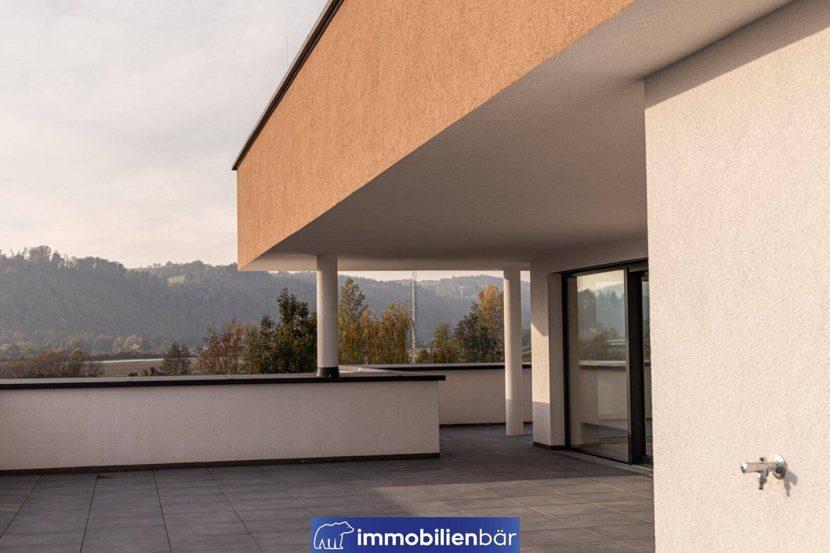 Überdachte Terrasse mit Säulen und weitem Blick auf die grüne Landschaft und Hügel.