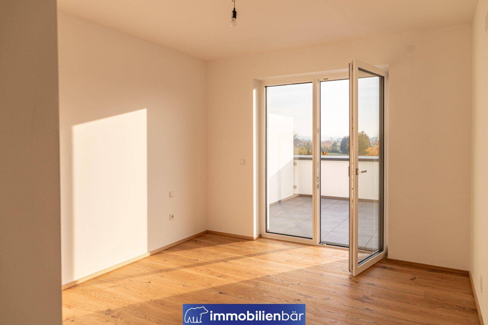 Heller Raum mit Holzboden und Fenstertür, die auf eine private Terrasse führt.