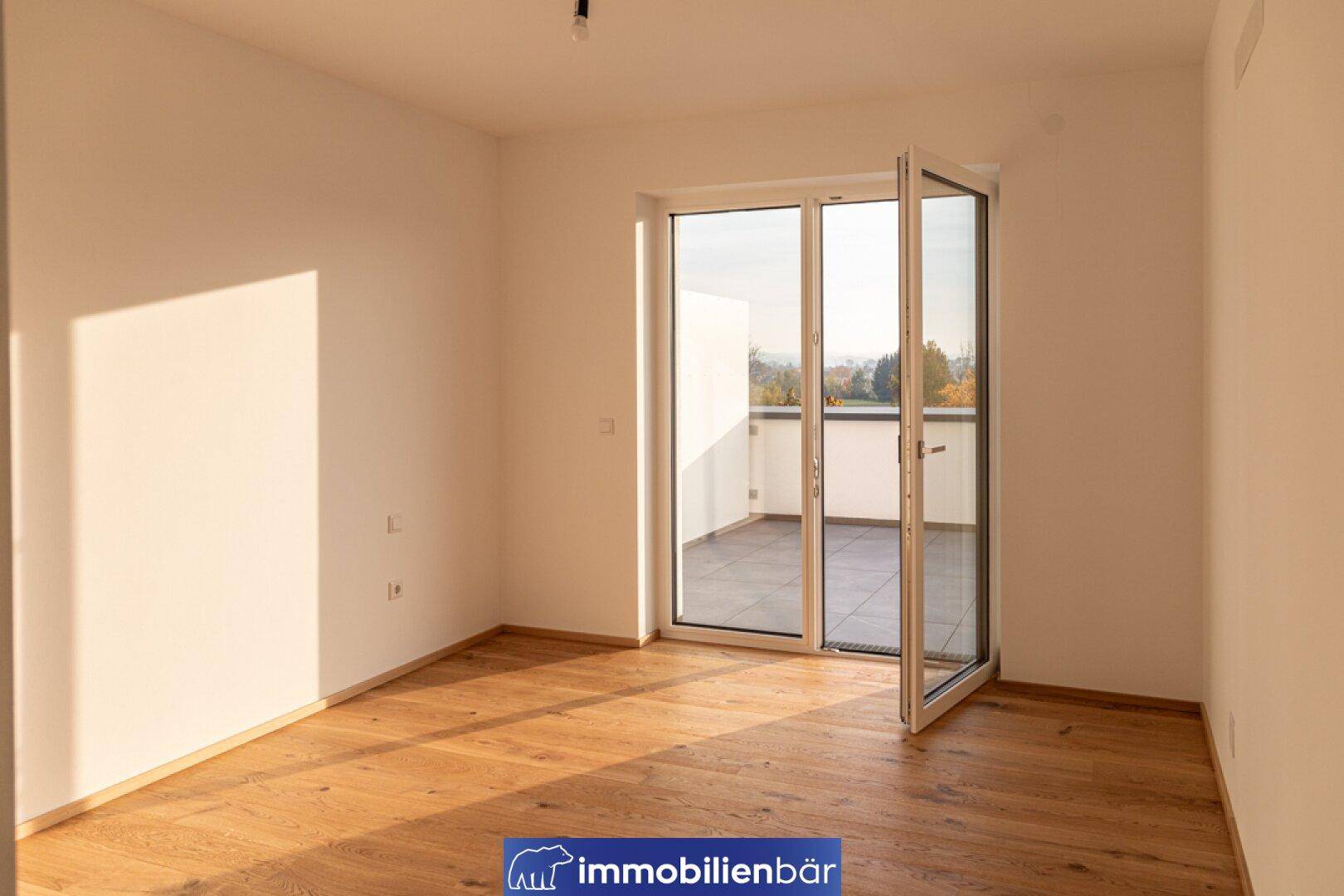 Sonniger Raum mit Holzboden und Fenstertür, die direkten Zugang zur Terrasse bietet.