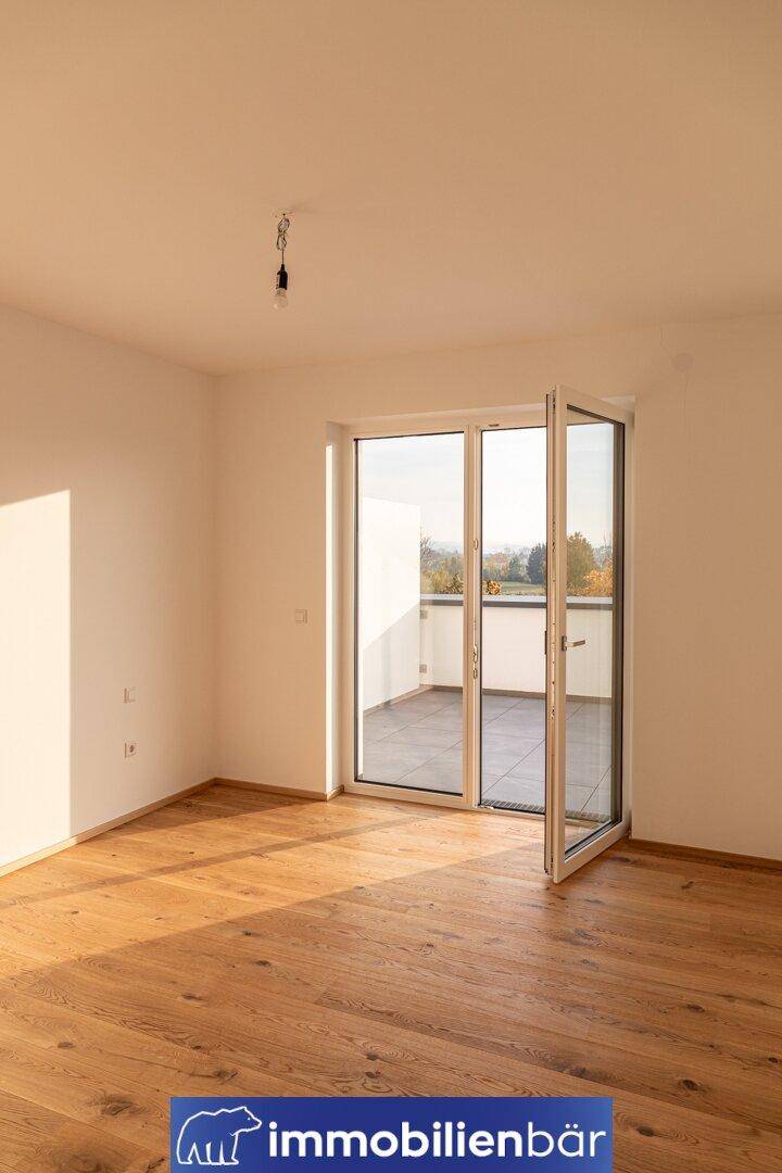 Helles Zimmer mit Holzboden und Fenstertür, die auf eine private Terrasse führt.