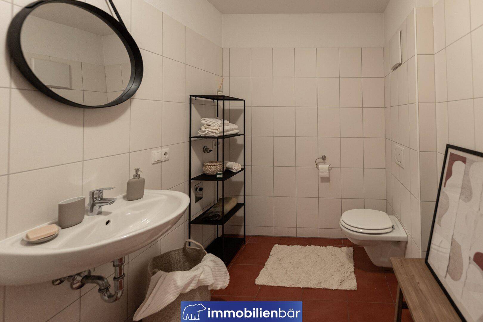 Modern eingerichtetes Badezimmer mit Waschbecken, WC und Spiegel, gefliest in Weiß und Terrakotta.