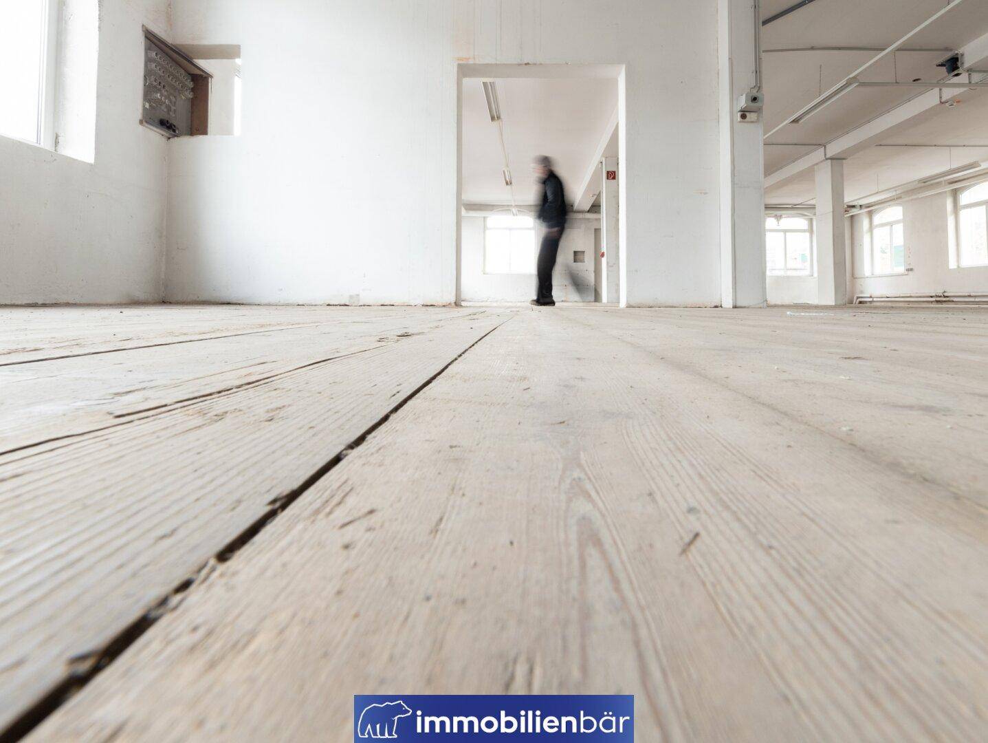 Nahaufnahme des abgenutzten Holzplankenbodens in einem großen, hellen Industrieraum.